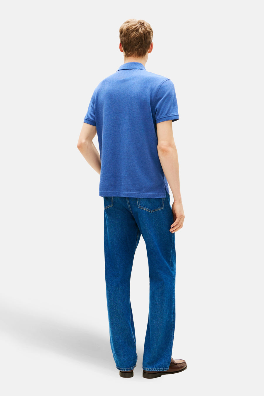 Polo à manches courtes bleu de TOMMY HILFIGER, porté avec un jean et des chaussures marron, vue de dos.
