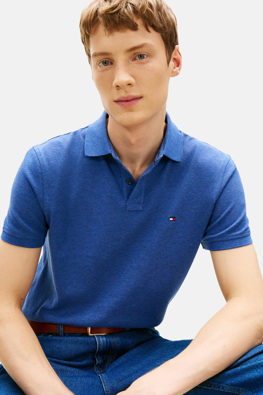 Polo bleu à manches courtes de Tommy Hilfiger, porté avec un jean et une ceinture marron.