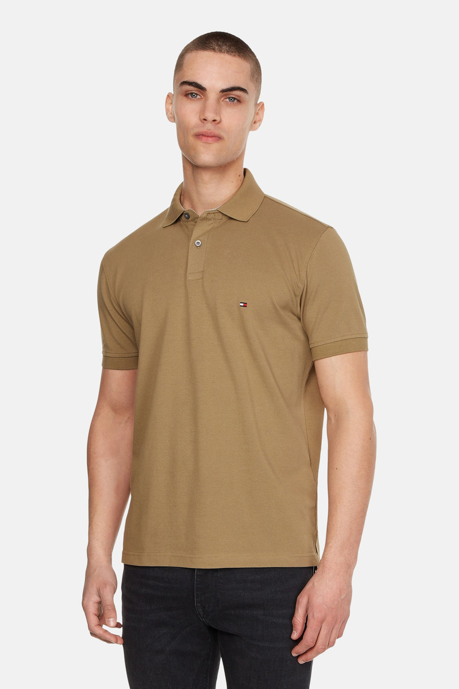 Polo kaki à manches courtes de TOMMY HILFIGER, porté avec un jean noir, sur fond blanc.