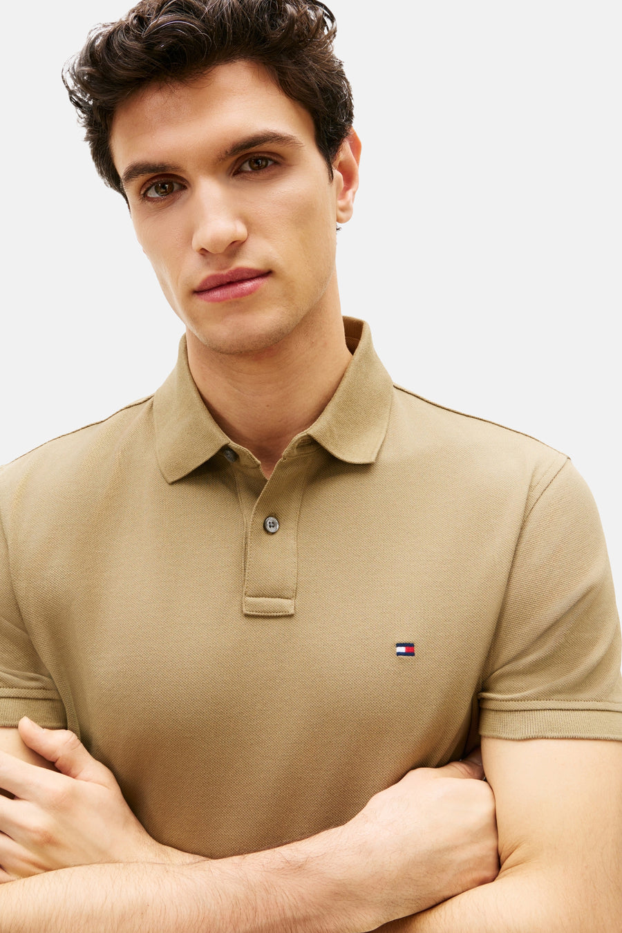 Polo kaki à manches courtes de Tommy Hilfiger, porté par un homme aux bras croisés.