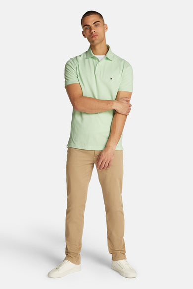 Polo à manches courtes vert par Tommy Hilfiger, porté avec un pantalon chino beige et des baskets blanches.