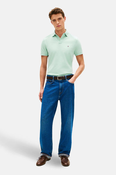 Polo vert à manches courtes de TOMMY HILFIGER, porté avec un jean bleu et des chaussures marron.