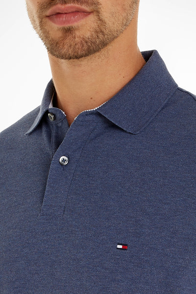 Navy blue polo shirt by Tommy Hilfiger, featuring ribbed collar, silver buttons, and small flag logo on chest, close-up front view