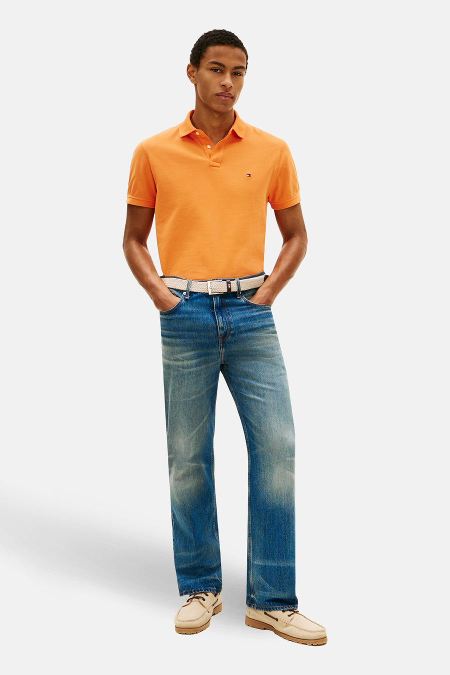 Polo orange à manches courtes de TOMMY HILFIGER, porté avec un jean bleu et des chaussures bateau beige.