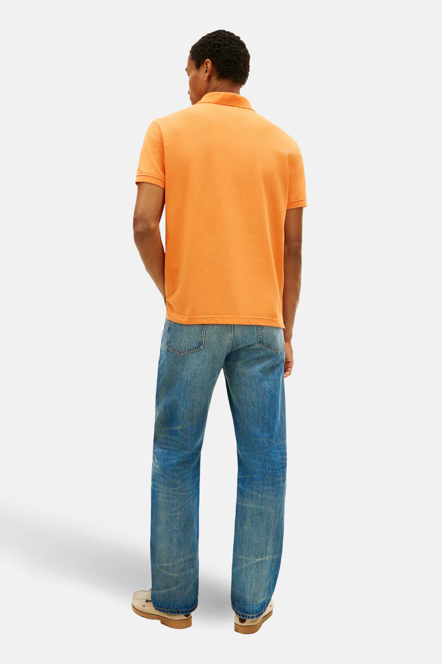Polo orange à manches courtes de TOMMY HILFIGER, porté avec un jean bleu et des chaussures bateau beiges, vue de dos.