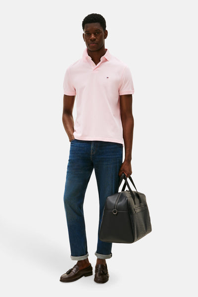 Polo à manches courtes rose de Tommy Hilfiger, porté avec un jean et des mocassins avec un sac de voyage noir.
