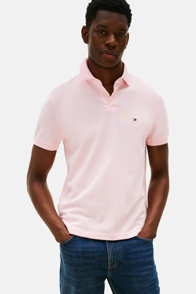Polo rose à manches courtes de Tommy Hilfiger, porté avec un jean bleu, les mains dans les poches.