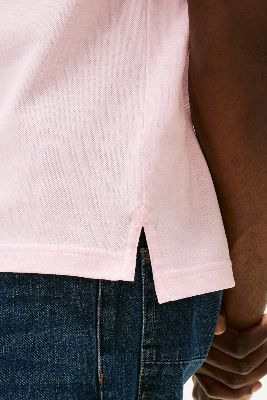 Polo rose à manches courtes de TOMMY HILFIGER, détail de l'ourlet fendu, porté avec un jean bleu.
