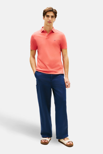 Polo à manches courtes rouge de TOMMY HILFIGER, porté avec un pantalon bleu ample et des sandales.
