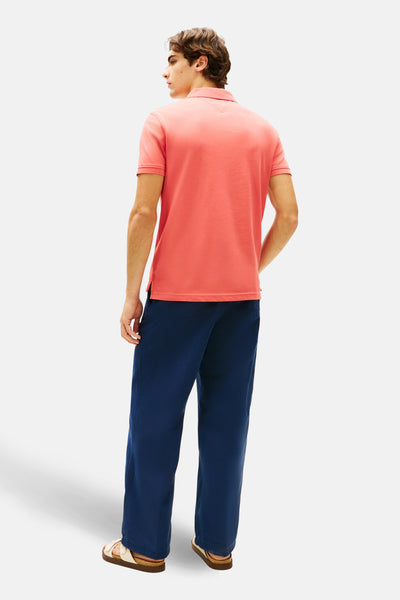 Polo à manches courtes rouge de TOMMY HILFIGER, porté avec un pantalon bleu marine et des sandales en cuir.