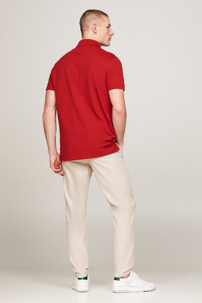 Polo rouge à manches courtes de TOMMY HILFIGER, porté avec un pantalon beige et des baskets blanches.