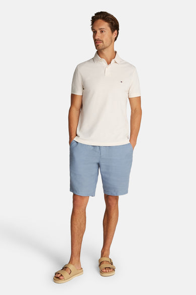 Polo à manches courtes écru de TOMMY HILFIGER, porté avec un short bleu en lin et des sandales.