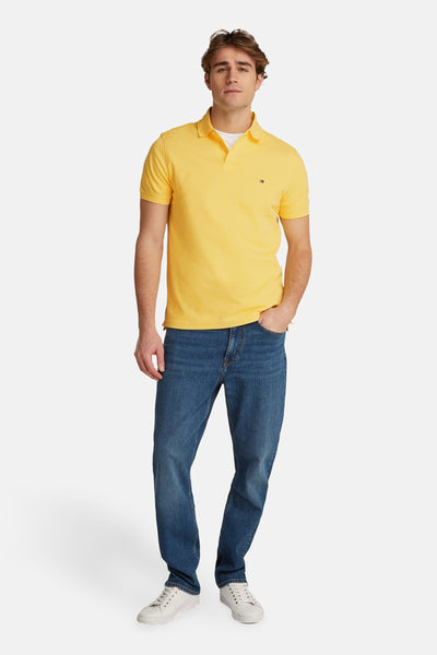 Geel polo van TOMMY HILFIGER gedragen met een blauwe broek en witte sneakers.