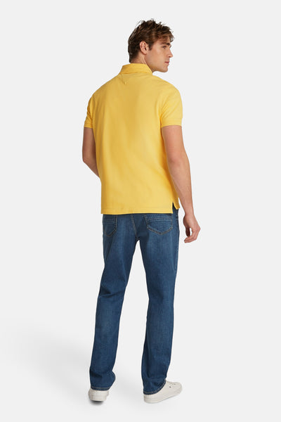 Geel polo van TOMMY HILFIGER, gedragen met een blauwe broek en witte schoenen.