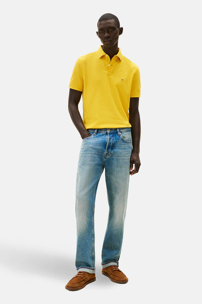 Polo à manches courtes jaune de Tommy Hilfiger, porté avec un jean bleu clair et des chaussures marron.