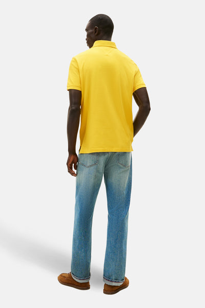 Polo à manches courtes jaune de TOMMY HILFIGER, porté avec un jean et des chaussures marron, vue de dos.