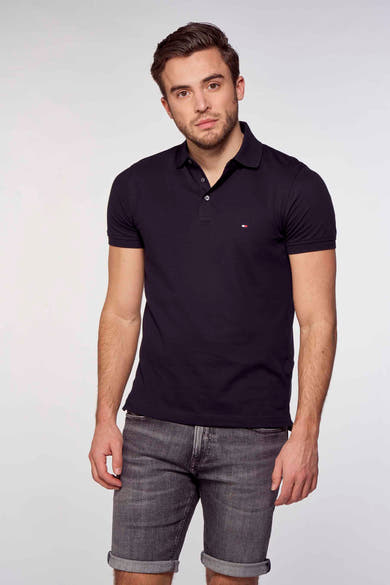 Polo bleu marine de Tommy Hilfiger, porté avec un short en jean gris délavé, sur fond blanc.