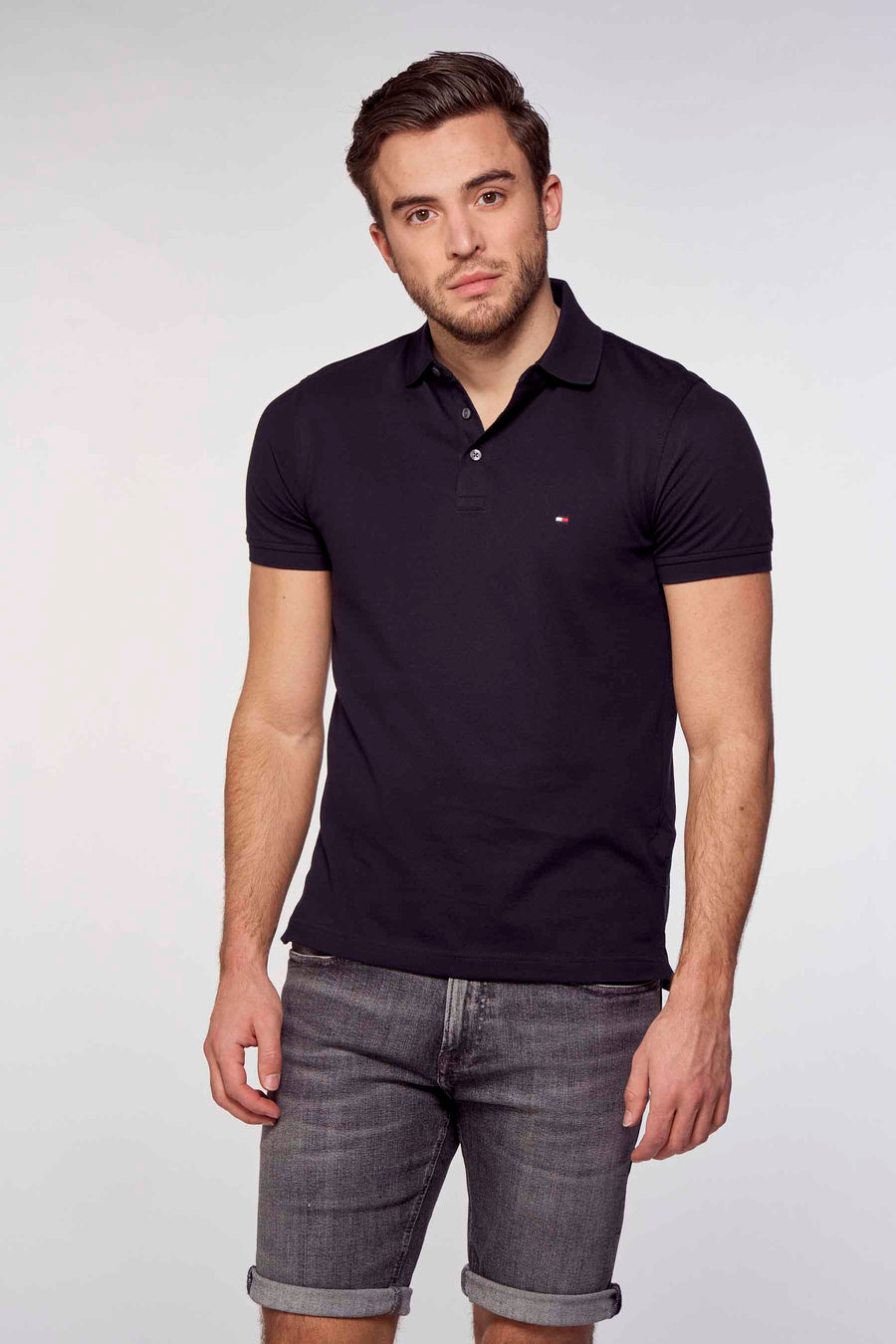Polo bleu marine de Tommy Hilfiger, porté avec un short en jean gris délavé, sur fond blanc.