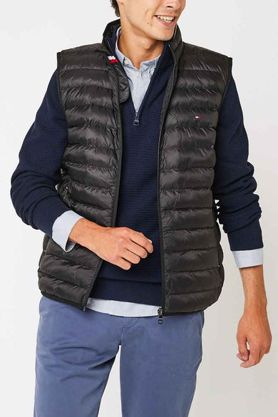 Veste sans manches noire de Tommy Jeans, portée sur un pull bleu marine et une chemise bleue, avec un pantalon bleu.
