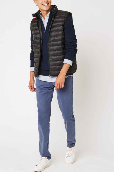 Veste sans manches noire de Tommy Jeans, portée sur un pull bleu marine, avec un pantalon bleu et des baskets blanches.