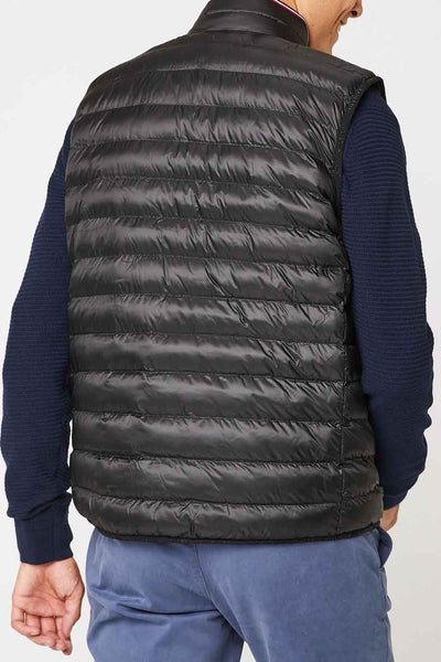 Veste sans manches noire de Tommy Jeans, portée avec un pull bleu marine et un pantalon bleu.