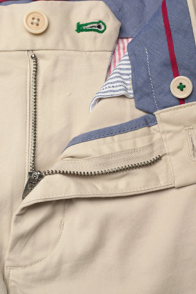 Beige cotton bermuda shorts with front zipper and button closure, featuring blue striped lining and green embroidered detail, close-up view