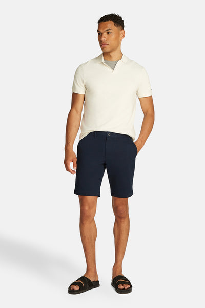 Marineblauwe bermuda van TOMMY HILFIGER, gedragen met een beige poloshirt en zwarte sandalen.