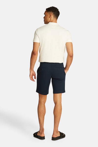 Blauwe bermuda van TOMMY HILFIGER, gedragen met een gebroken witte polo en zwarte sandalen.