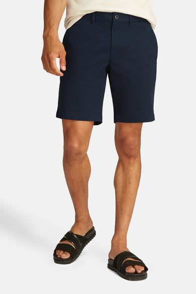 Blauwe bermuda van TOMMY HILFIGER, gedragen met zwarte sandalen en een beige T-shirt.