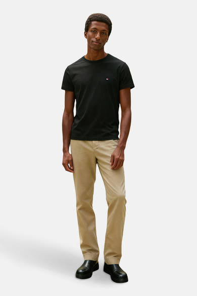 T-shirt noir à manches courtes de TOMMY HILFIGER, porté avec un pantalon beige et des chaussures noires.