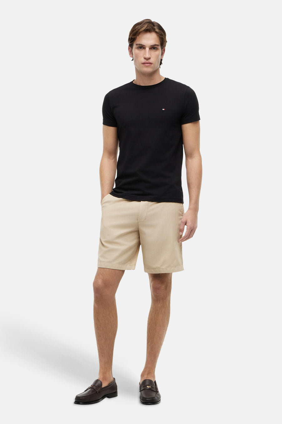 T-shirt à manches courtes noir de Tommy Hilfiger, porté avec un short beige et des mocassins marron.
