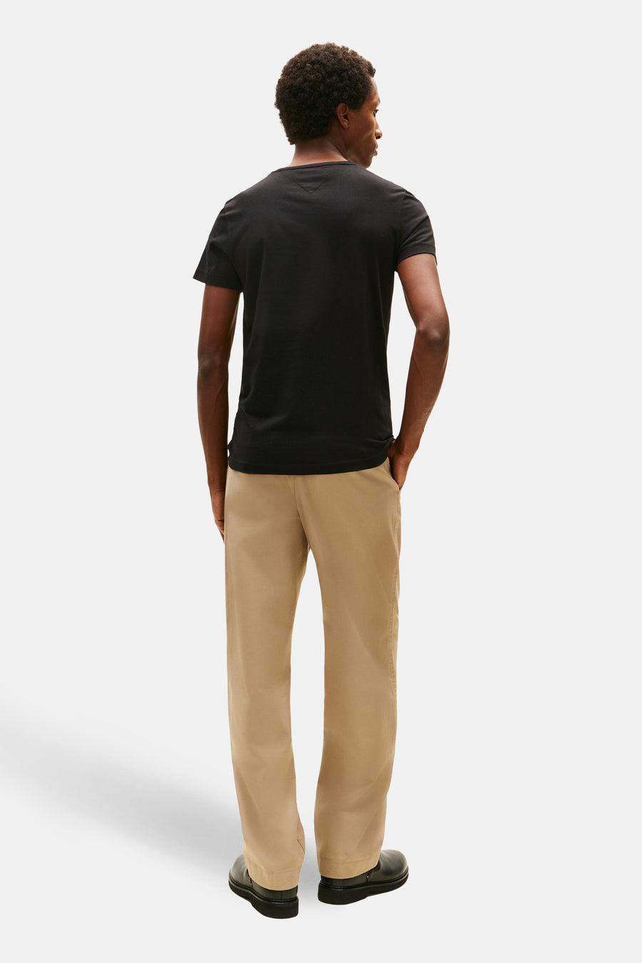 T-shirt à manches courtes noir de TOMMY HILFIGER, vu de dos, porté avec un pantalon beige et des chaussures noires.
