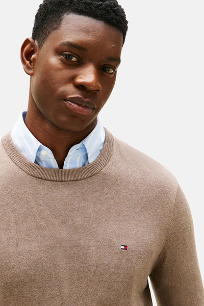 Pull beige à col rond de TOMMY HILFIGER, porté sur une chemise rayée bleu clair.