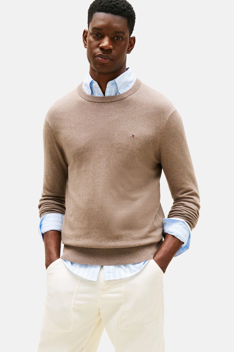 Beige ronde hals trui van TOMMY HILFIGER, gedragen over een blauw gestreept overhemd en een witte broek.