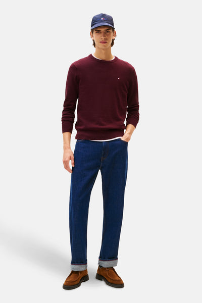 Bordeaux ronde hals trui van Tommy Hilfiger, gedragen met een blauwe jeans en bruine schoenen.