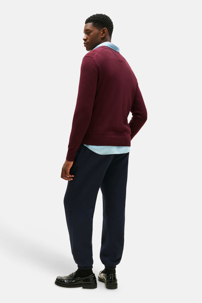 Bordeaux V-hals trui van TOMMY HILFIGER, gedragen over een lichtblauw overhemd en een marineblauwe joggingbroek.