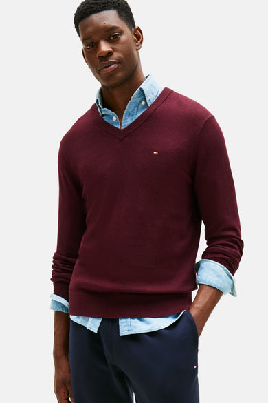 Bordeaux V-hals trui van TOMMY HILFIGER, gedragen over een spijkerblouse, met een marineblauwe broek.