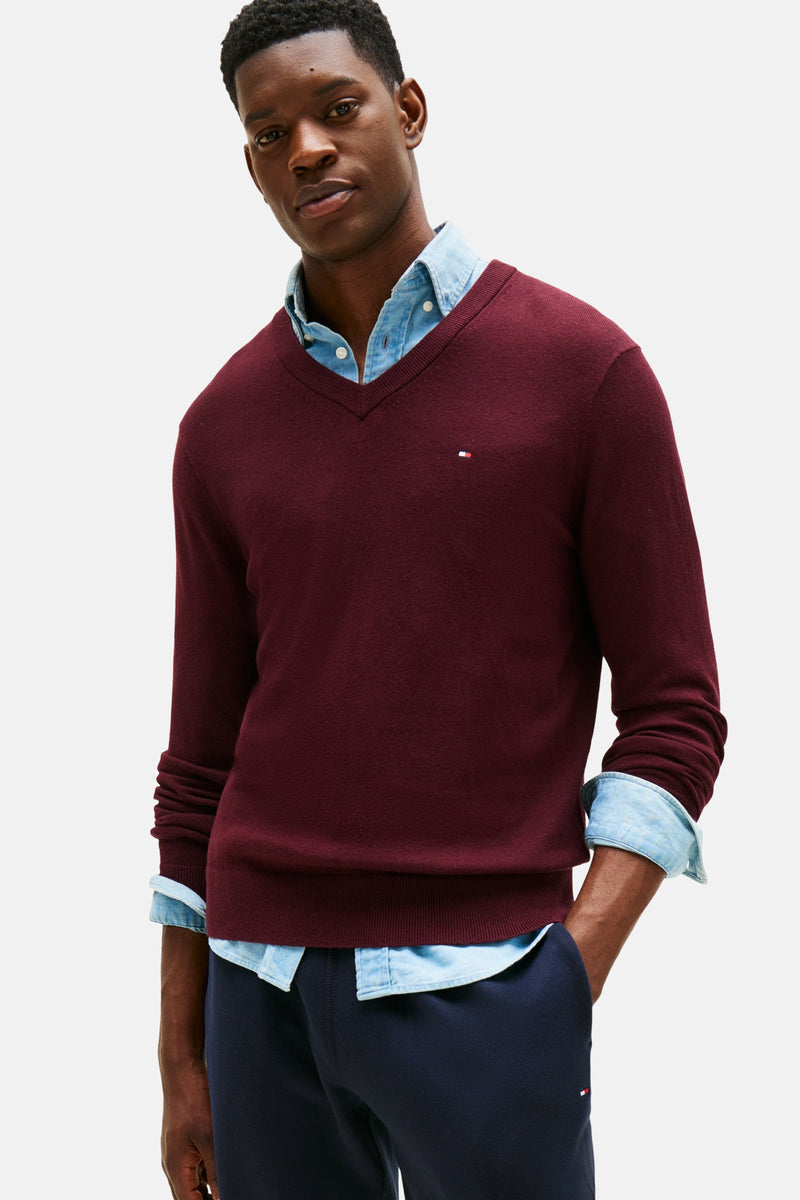 Bordeaux V-hals trui van TOMMY HILFIGER, gedragen over een spijkerblouse, met een marineblauwe broek.