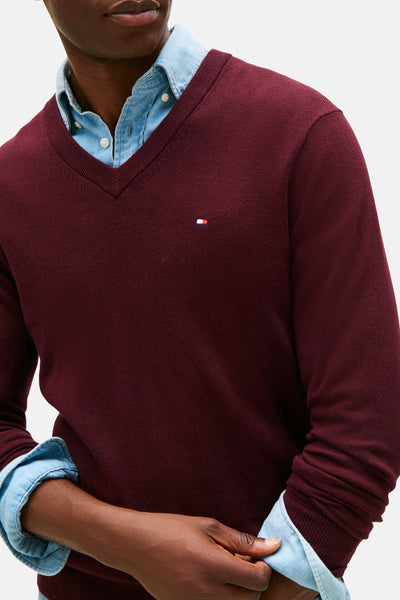 Pull à col en V bordeaux de TOMMY HILFIGER, porté sur une chemise en jean bleu clair.
