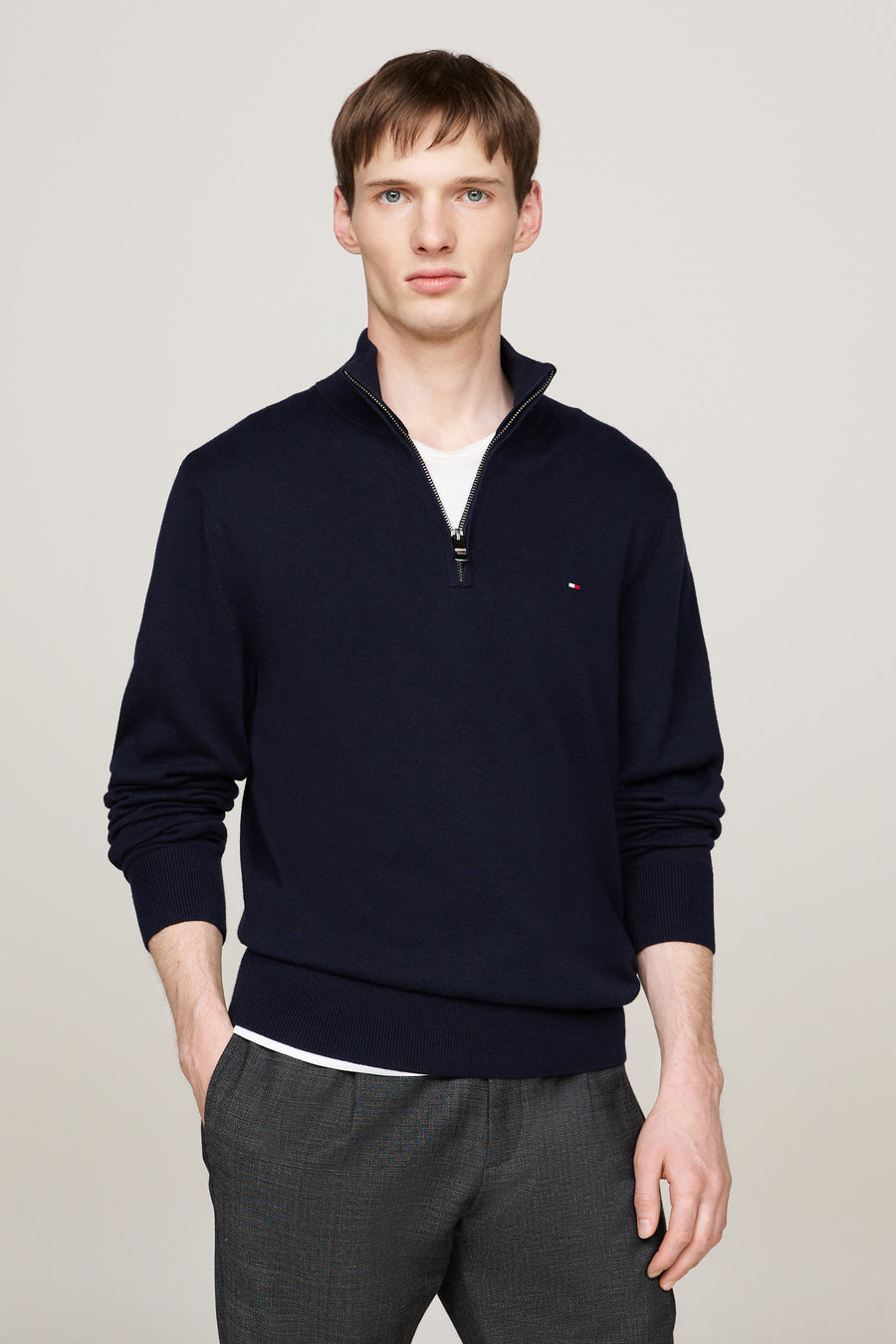 Pull à col roulé bleu de TOMMY HILFIGER, porté sur un t-shirt blanc avec un pantalon gris.