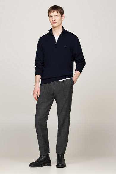 Pull bleu à col zippé de Tommy Hilfiger porté avec un pantalon gris à motifs et des bottines noires.