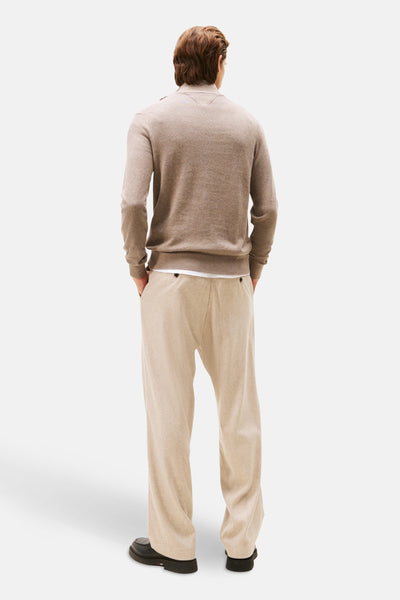 Pull à col roulé beige de TOMMY HILFIGER, porté avec un pantalon ample clair et des chaussures noires, vue de dos.