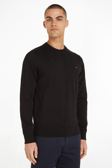 Pull col rond noir de TOMMY HILFIGER, porté avec un pantalon marine uni.