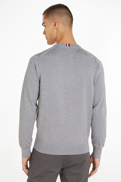 Pull col rond gris de Tommy Hilfiger, avec rayures iconiques au col et porté avec un pantalon gris.