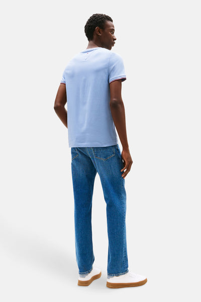 Blauw T-shirt met korte mouwen van Tommy Hilfiger, met rode randen aan de mouwen, gedragen met een spijkerbroek en witte sneakers.