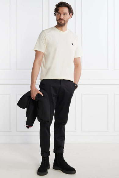 Ecru short-sleeve t-shirt with small black logo on chest, worn by model with black pants and boots, full-body lifestyle view