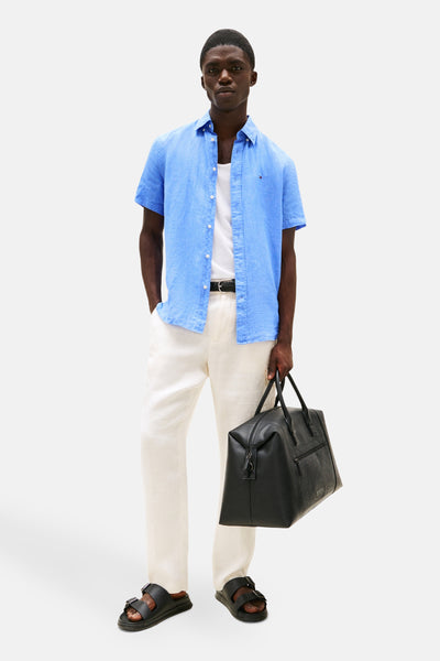 Chemise à manches courtes bleue en lin de TOMMY HILFIGER, portée avec un débardeur blanc et un pantalon blanc.