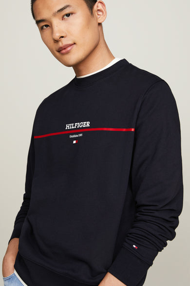 Sweat-shirt bleu marine par Tommy Hilfiger avec logo sur la poitrine et drapeau sur la manche.