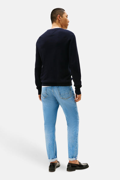 Pull à col rond bleu de TOMMY HILFIGER, porté avec un jean bleu clair et des mocassins noirs.
