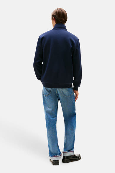 Sweat bleu foncé de TOMMY HILFIGER, porté avec un jean délavé aux ourlets repliés et des mocassins noirs.